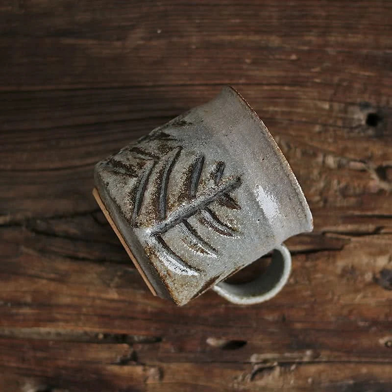 Handmade ceramic coffee mug with rustic leaf design on wooden surface. Vintage style drinkware.